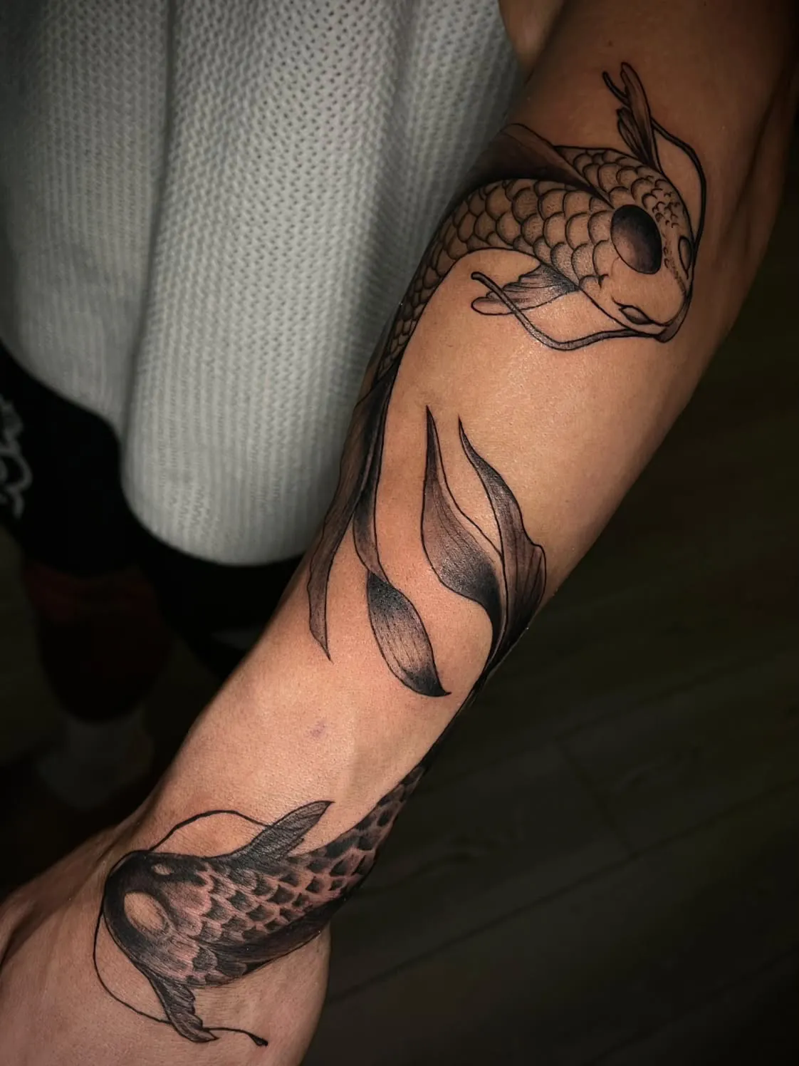 Two koi with flowing fins circling the forearm from the inner elbow to the wrist