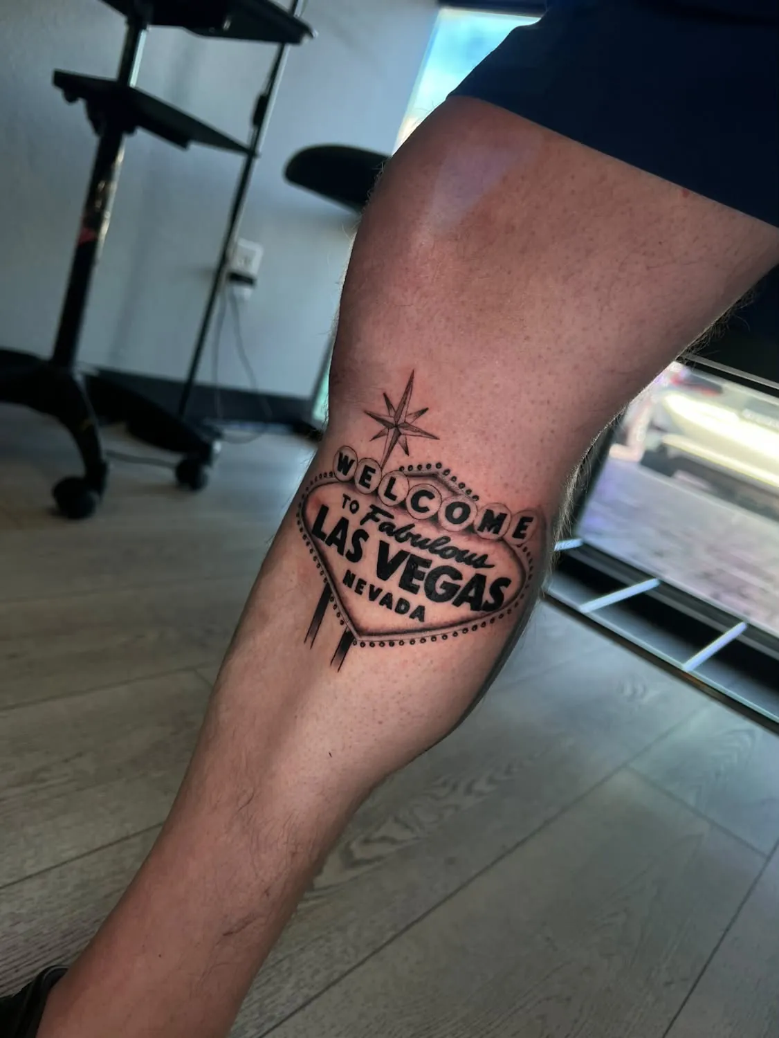 Black-and-gray tattoo of the Welcome to Fabulous Las Vegas sign with its star and bulb border on the back of the leg