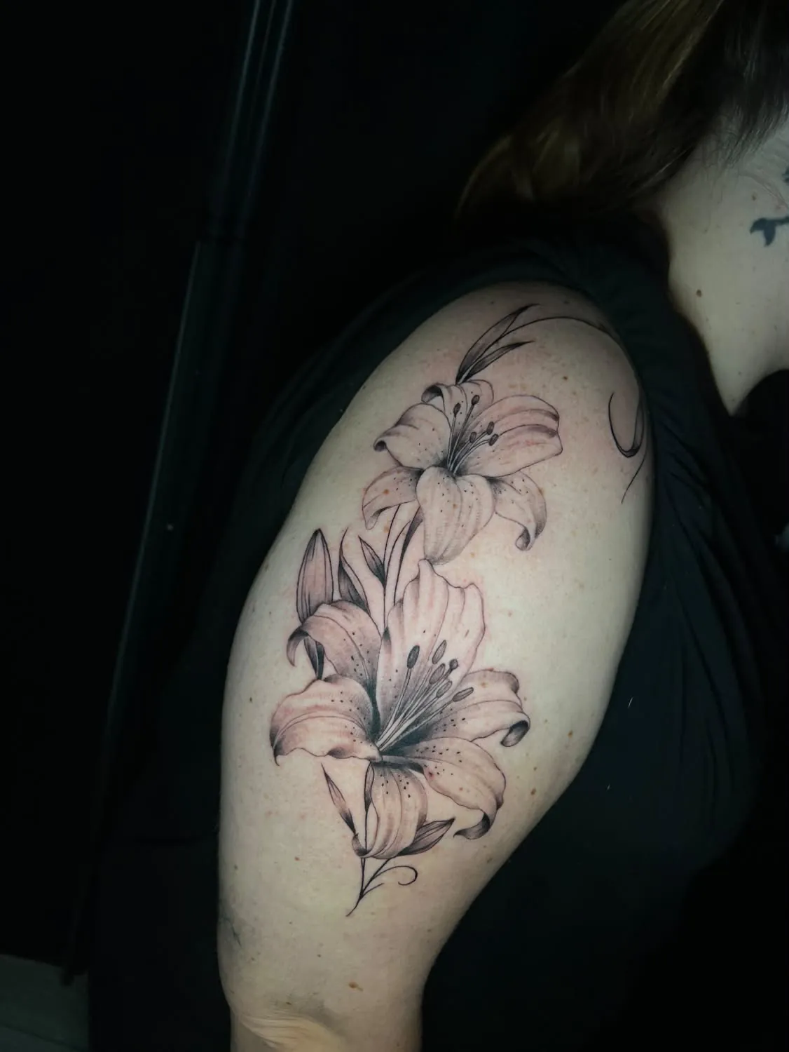 Two soft-shaded lilies with buds and stems climbing the outer upper arm