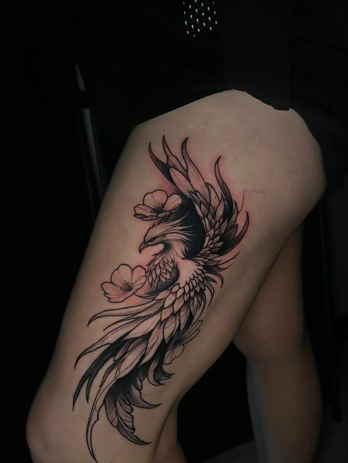 Black-and-gray phoenix with open blossoms, its long tail feathers flowing down the outer thigh