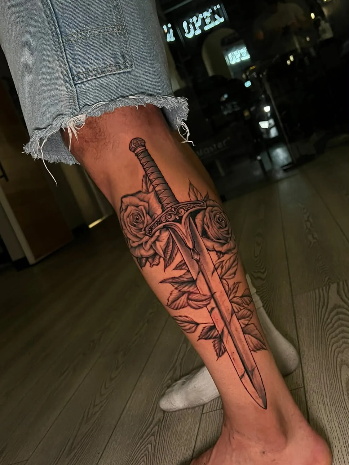 Detailed sword with an engraved crossguard running down the calf through two roses and leaves